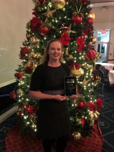 Colleen Nicoulin holding an award in front of a Christmas tree