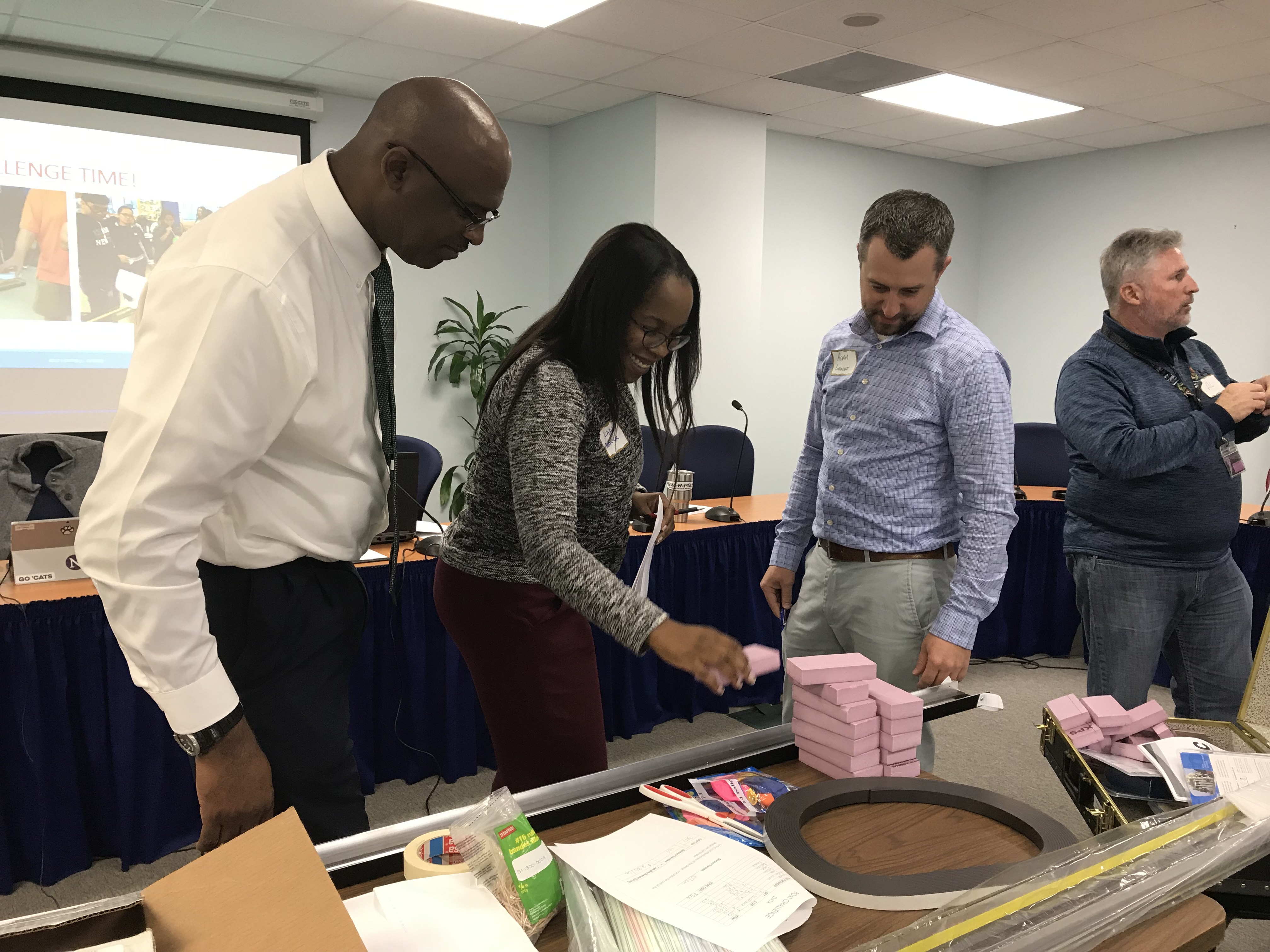 Four people (3 men and one woman) looking at pink Styrofoam bricks in the TPO Conference Room