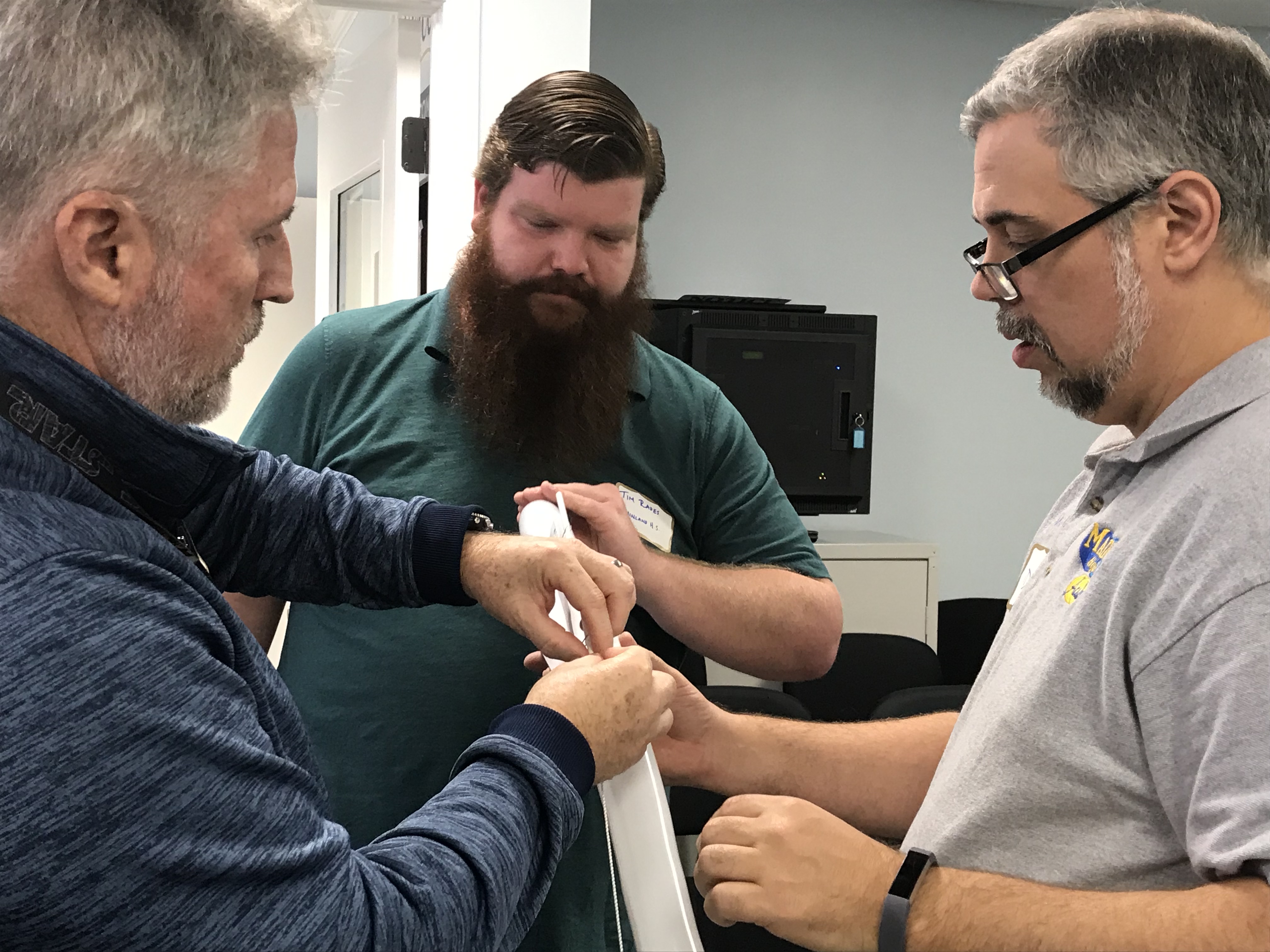 Three male teachers looking at a long metal track that is facing downward