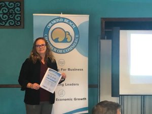Colleen Nicoulin posing in front of the Chamber of Commerce Sign